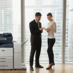 Two people in an office in business attire discussing documents stand by a Xerox® AltaLink® B8200 Series Multifunction Printer Two people in an office in business attire discussing documents stand by a Xerox® AltaLink® B8200 Series Multifunction Printer