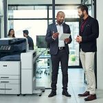 Two men in an office setting discussing something on a tablet beside a Xerox® AltaLink® C8200 Series Colour Multifunction Printer Two men in an office setting discussing something on a tablet beside a Xerox® AltaLink® C8200 Series Colour Multifunction Printer