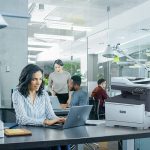 Xerox® C325 Colour Multifunction Printer in an office situation Professional woman typing on laptop at desk in office environment next to a Xerox® C325 Printer